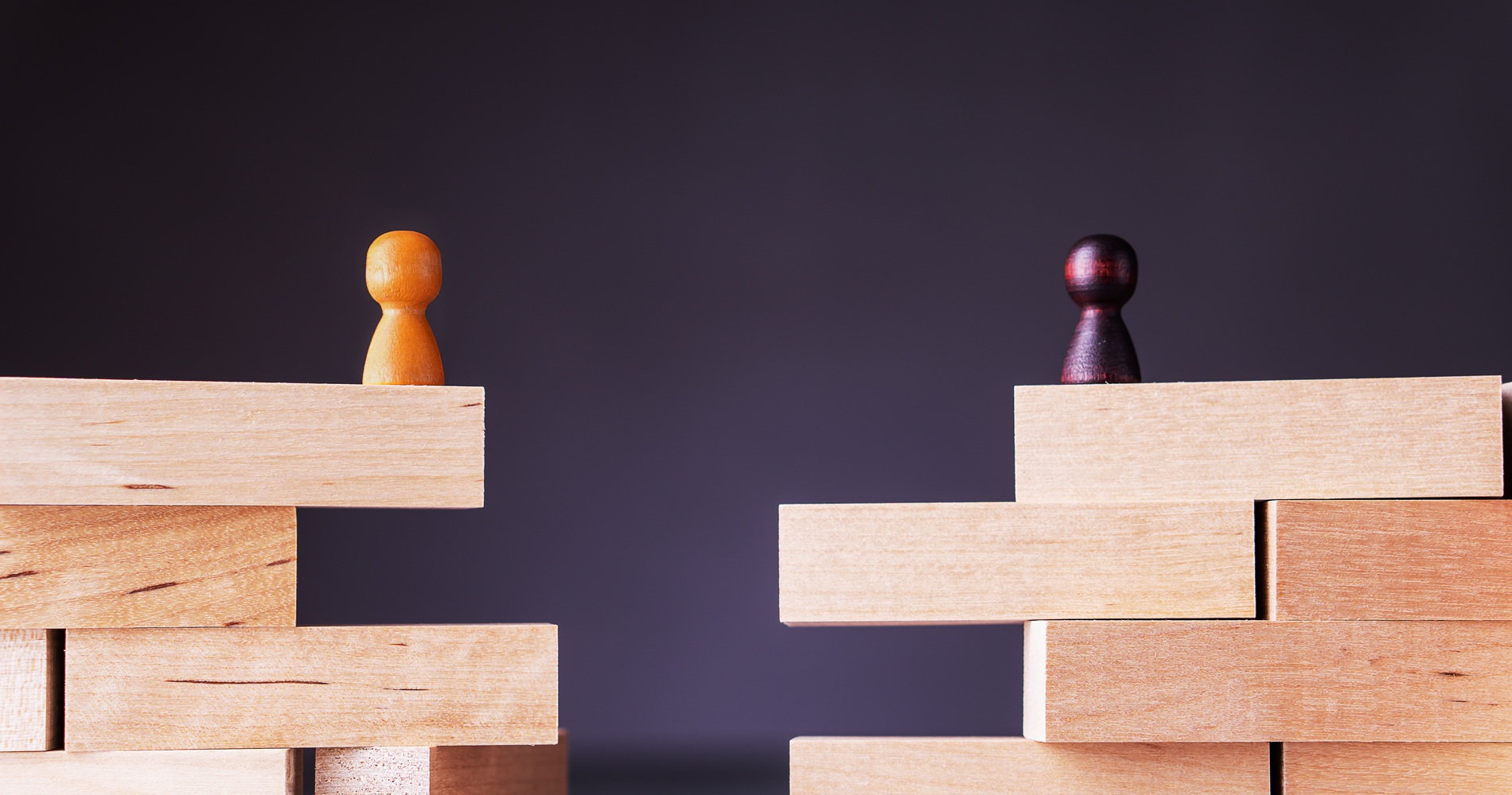 Two wooden block structures with separated pawn figures, symbolizing organizational division, cultural distance, or merger integration challenges.